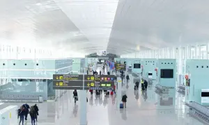 Jasny, przestronny terminal lotniska Barcelona El Prat z podróżnymi i tablicami kierunkowymi.
