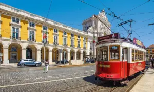 Czerwony tramwaj w Lizbonie, obok żółtego budynku z arkadami. Czy do Portugalii potrzebny jest paszport? Warto sprawdzić przed podróżą!