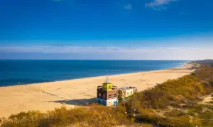 Słoneczna jelitkowo plaża z charakterystycznym budynkiem i morzem w tle.