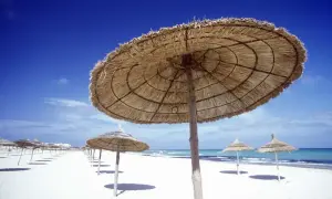 Słomiane parasole na białej plaży, idealne na tunezja wakacje. Błękitne niebo i morze zapraszają do odpoczynku.