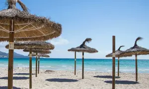 Słomiane parasole na piaszczystej plaży nad turkusową wodą, idealne na wakacje w zatoce alkudyjskiej.