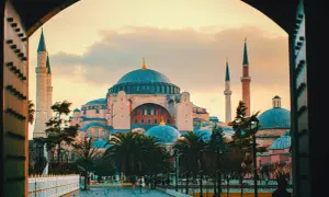 Majestatyczna Hagia Sophia z kopułami i minaretami, otoczona palmami, w blasku zachodzącego słońca.