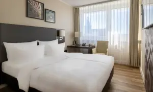 Przytulny pokój w hotelu Radisson Blu Erfurt z białym pościelonym łóżkiem, biurkiem i oknem z widokiem na miasto.