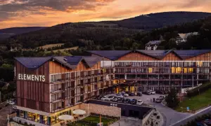 Nowoczesny hotel 5 gwiazdkowy "Elements" w otoczeniu górskiego krajobrazu, z widokiem na las i zachodzące słońce.
