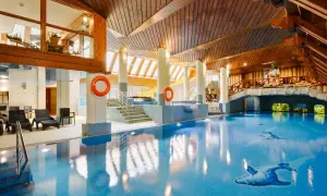 Basen w hotelu Belvedere Resort & Spa z drewnianym sufitem i mostkiem. Woda jest błękitna, a na dnie widać ozdobne ryby.