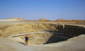 Mężczyzna stoi na krawędzi gigantycznego krateru na pustyni Karakum.