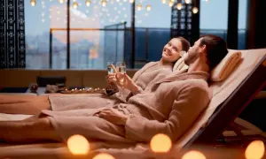 Para relaksu w hotelach dla dorosłych: para w szlafrokach wznosi toasty szampanem, otoczona świecami i widokiem na miasto.