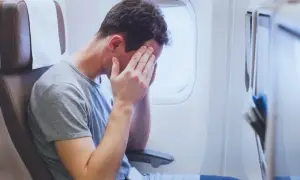 Mężczyzna w samolocie z rękami na twarzy, cierpiący na jetlag. To uczucie zmęczenia i dezorientacji po podróży.