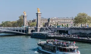 Rejs po Sekwanie w Paryżu. Statek wycieczkowy z turystami płynie obok mostu z rzeźbami.