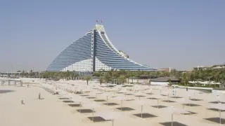 Pusta plaża z rzędami parasoli i charakterystycznym budynkiem hotelu w tle. Ceny w Dubaju mogą być wysokie, ale widoki są niezapomniane.