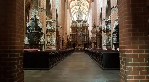 Wnętrze katedry w Pelplinie z rzędami ławek i bogato zdobionym ołtarzem głównym.
