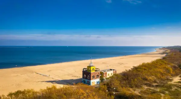 Słoneczna jelitkowo plaża z charakterystycznym budynkiem i morzem w tle.