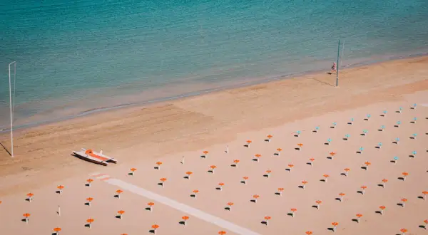 Pusta plaża w Rimini z rzędem pomarańczowych parasoli i łodzią motorową.