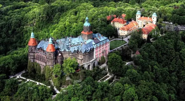 Zamek **Chudów** otoczony bujną zielenią, z charakterystycznymi wieżami i czerwonymi dachami, wygląda jak z bajki.