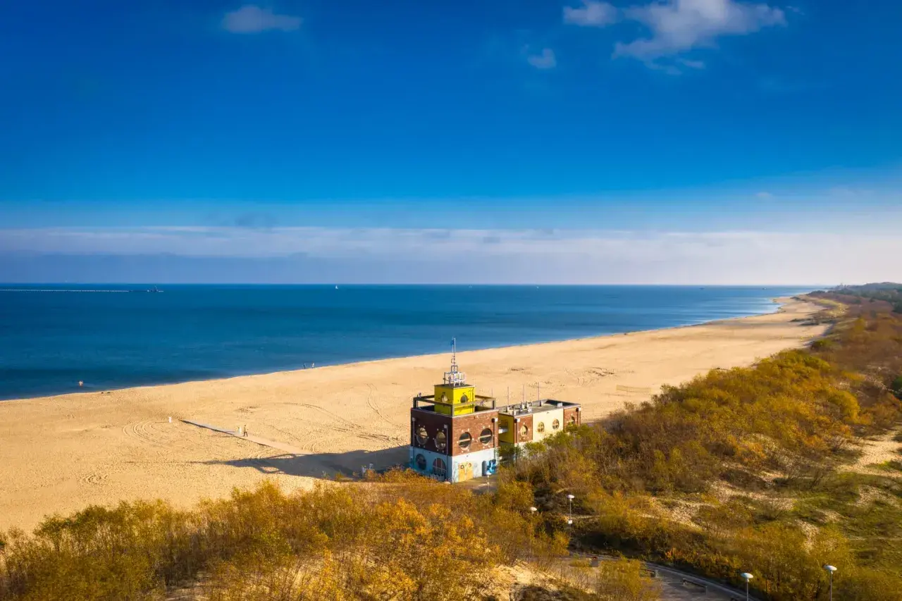 Słoneczna jelitkowo plaża z charakterystycznym budynkiem i morzem w tle.