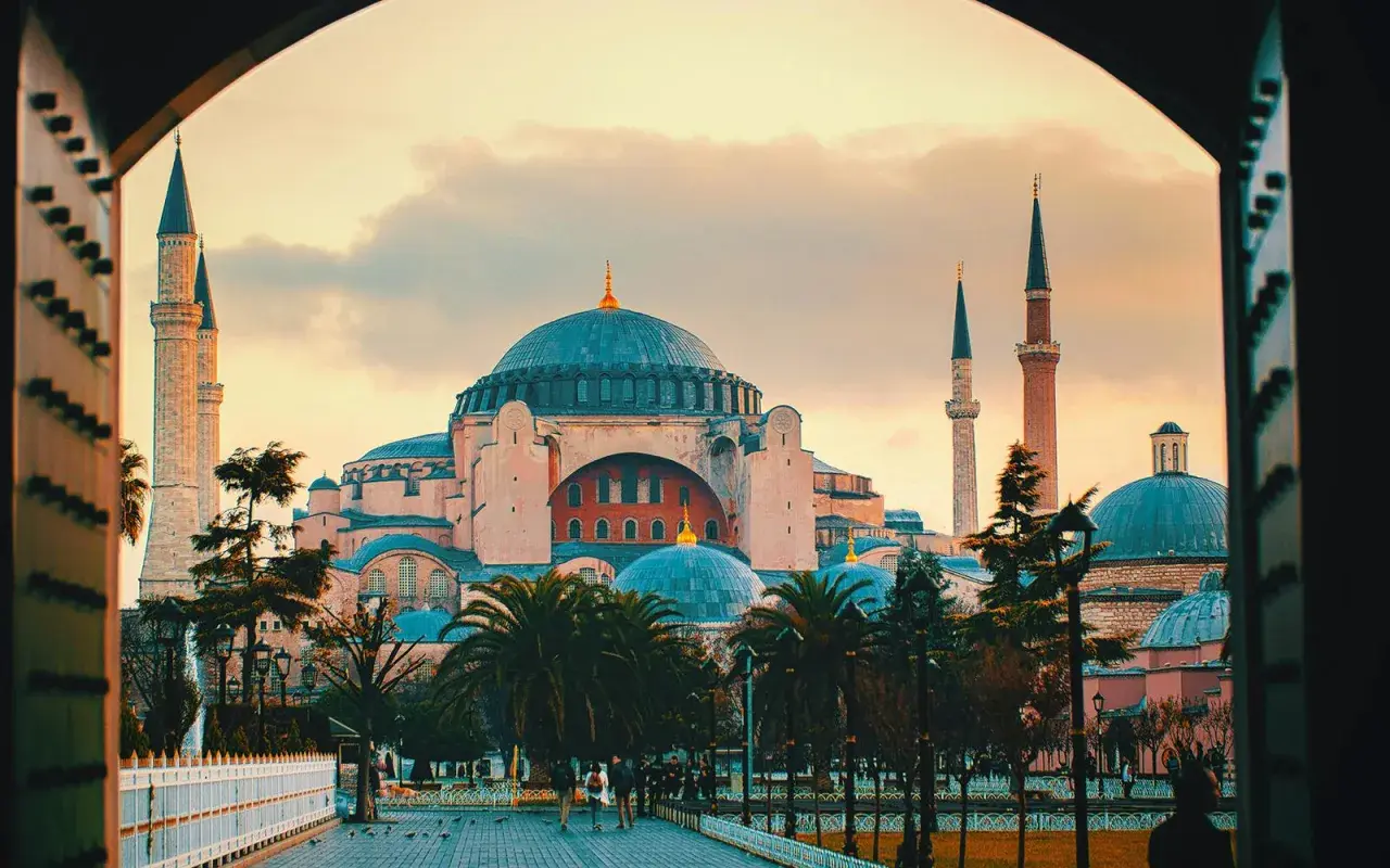 Majestatyczna Hagia Sophia z kopułami i minaretami, otoczona palmami, w blasku zachodzącego słońca.