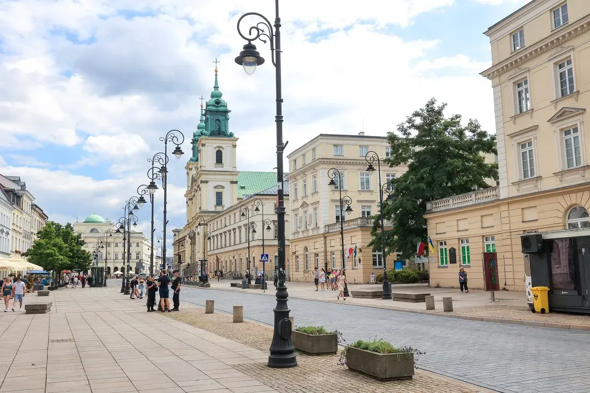 Spacer po Krakowskim Przedmieściu w Warszawie, z zabytkowymi kamienicami i kościołem w tle.