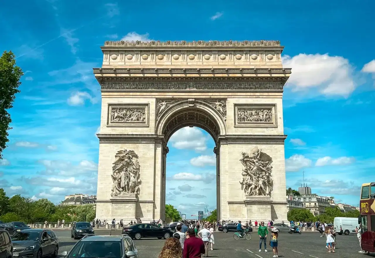 Łuk Triumfalny w Paryżu, symbol chwały, góruje nad ruchem ulicznym. Widok przez łuk przypomina spacer po Polach Elizejskich.