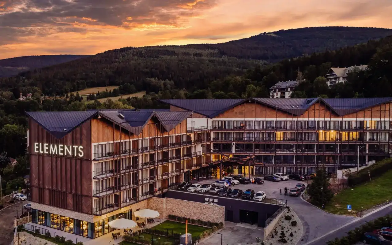 Nowoczesny hotel 5 gwiazdkowy "Elements" w otoczeniu górskiego krajobrazu, z widokiem na las i zachodzące słońce.