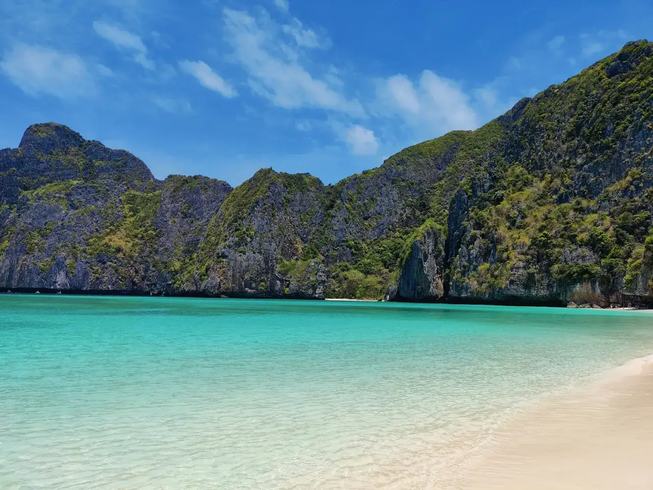 Rajska plaża Maya Bay z turkusową wodą i skalistymi górami porośniętymi zielenią.