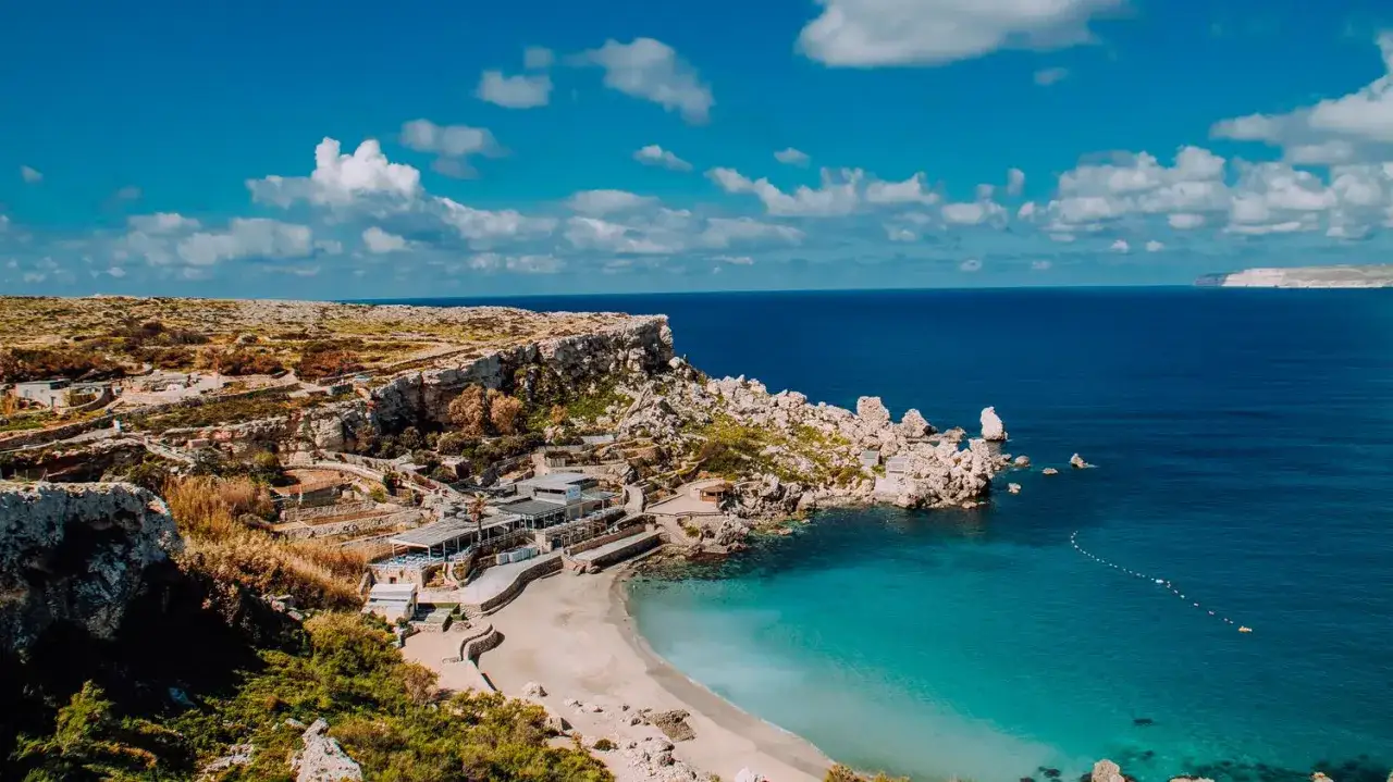 Malta wakacje: malownicza zatoka z turkusową wodą, skaliste klify i zabudowania przy plaży. Idealne miejsce na wypoczynek.