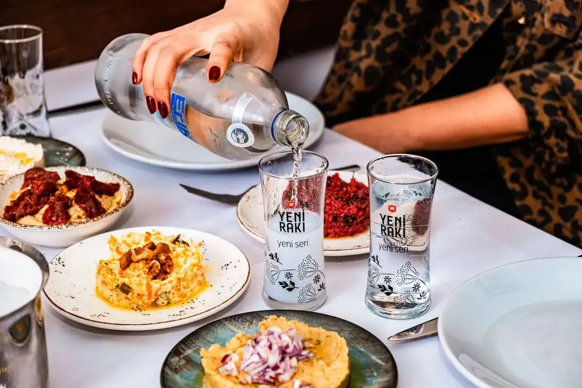 Nalewanie Yeni Raki do kieliszków, obok przystawek. Ten tradycyjny alkohol to idealny dodatek do tureckich smaków.