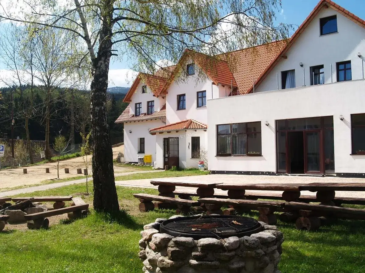 Wypoczynek w Jagniątkowie: białe budynki z czerwonymi dachami, drewniane ławy i grill na trawie.