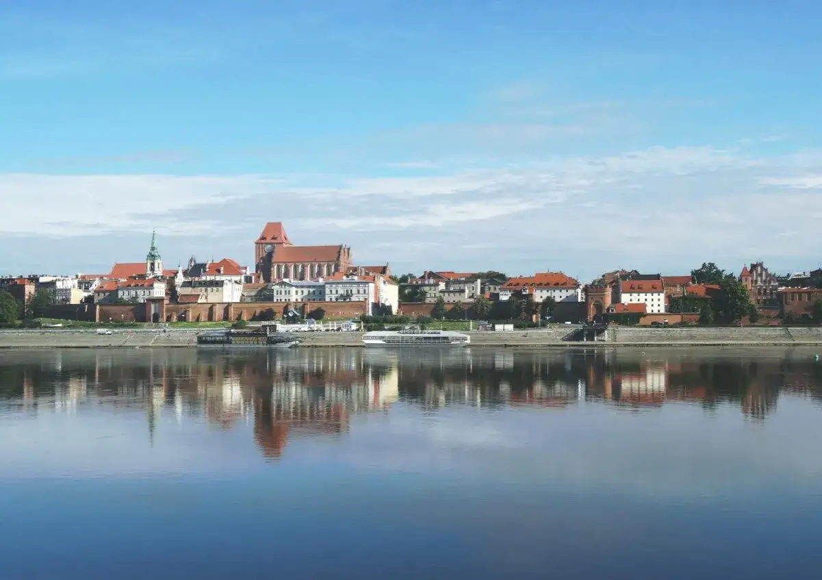 Widok na zabytkowe kamienice i katedrę w Toruniu, odbijające się w spokojnej tafli Wisły. Toruń stare miasto zachwyca o poranku.