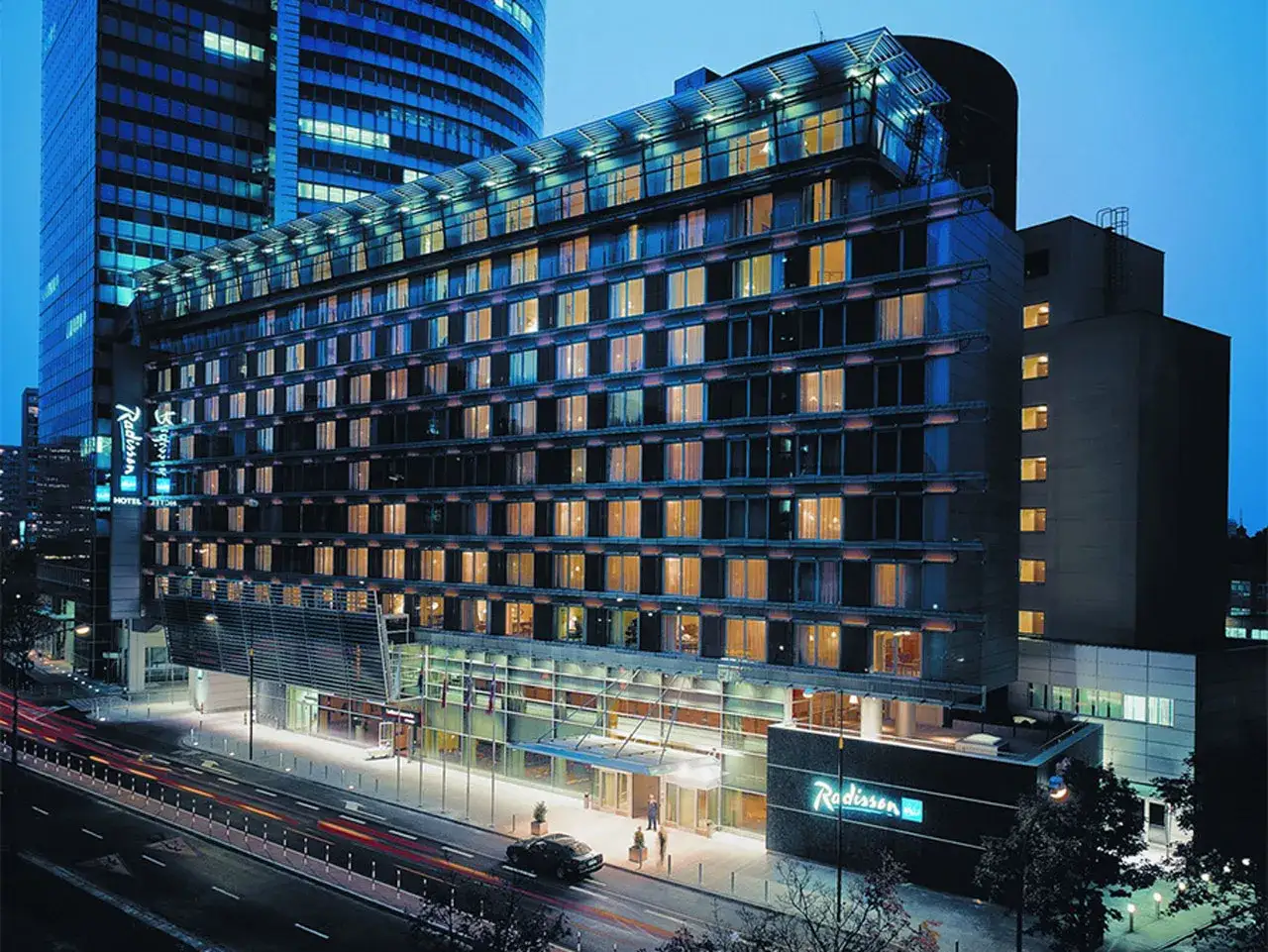 Radisson Collection Hotel Warsaw nocą, z oświetlonymi oknami i neonem hotelu.