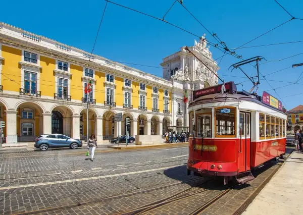 Czerwony tramwaj w Lizbonie, obok żółtego budynku z arkadami. Czy do Portugalii potrzebny jest paszport? Warto sprawdzić przed podróżą!