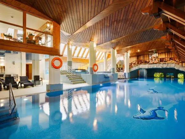 Basen w hotelu Belvedere Resort & Spa z drewnianym sufitem i mostkiem. Woda jest błękitna, a na dnie widać ozdobne ryby.