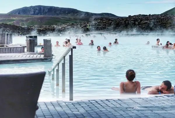 Ludzie relaksują się w turkusowej wodzie Blue Lagoon, otoczeni parującym krajobrazem i skalistymi wzgórzami.