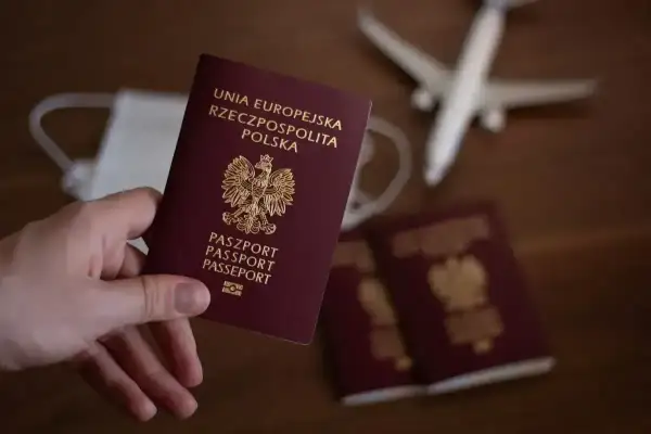 Dłoń trzyma polski paszport. Obok leżą inne paszporty, maseczka i samolot. Zastanawiasz się, ile wyrabia się paszport?